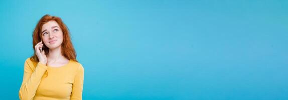 Lifestyle concept - Portrait of ginger red hair girl with shocking and stressful expression while talking with friend by mobile phone. Isolated on Blue Pastel Background. Copy space photo