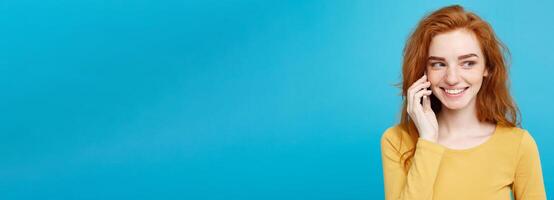 Lifestyle and Technology concept - Portrait of cheerful happy ginger red hair girl with joyful and exciting talking with friend by mobile phone. Isolated on Blue Pastel Background. Copy space. photo