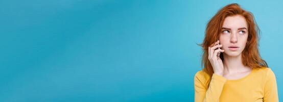 Lifestyle concept - Portrait of ginger red hair girl with shocking and stressful expression while talking with friend by mobile phone. Isolated on Blue Pastel Background. Copy space photo