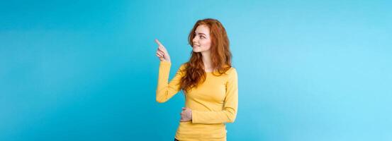 Close up Portrait young beautiful attractive redhair girl happy with something and pointing finger. Blue Pastel Background. Copy space photo