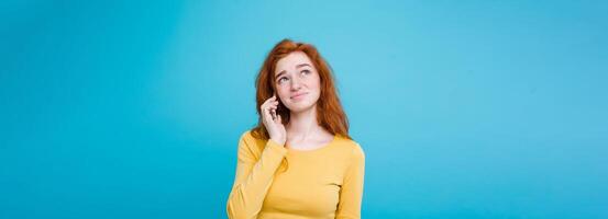 Lifestyle concept - Portrait of ginger red hair girl with shocking and stressful expression while talking with friend by mobile phone. Isolated on Blue Pastel Background. Copy space photo