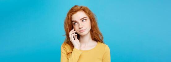 Portrait of ginger red hair girl with shocking and stressful expression while talking with friend by mobile phone. Isolated on Blue Pastel Background. Copy space. photo