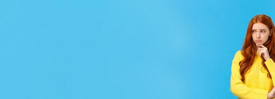 Sad timid and lonely redhead woman too feeling let down and depressed, sulking looking upset and envy left, frowning touching lip pensive, having bad feeling, standing anxious over blue background photo