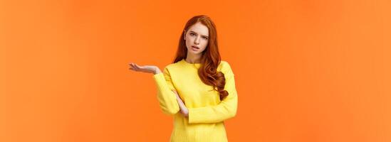 Skeptical and troubled, uncertain young redhead woman cant understand how resolve proble, shrugging raise hands sideways, frowning confused or unsure, standing frustrated orange background photo