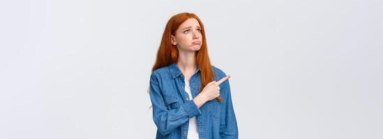 So pity. Upset gloomy cute redhead female student lost her chance participate exchange program, sobbing and looking grumpy pointing upper left corner, express regret and disappointment photo