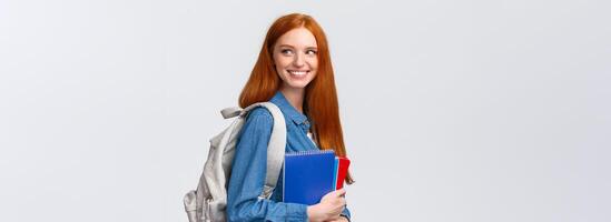 Girl seeing classmate in hall saying hi, turning back to greet someone, smiling joyfully, holding backpack and notebooks, heading back to class, studying in college, standing white background photo