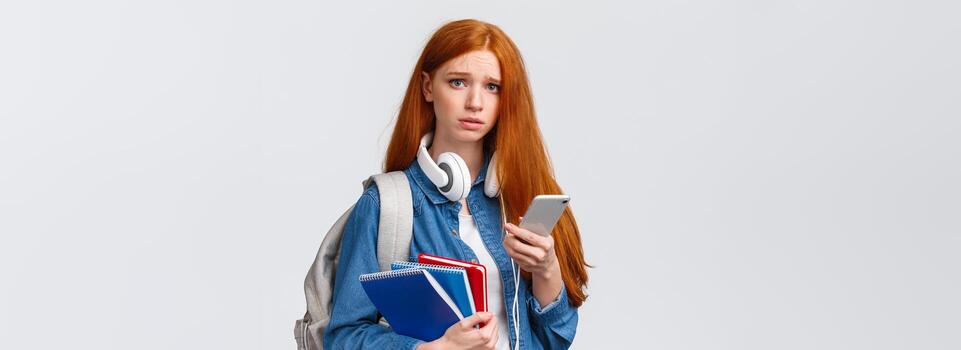 difícil, trastornado y melancólico linda pelirrojo Adolescente chica, estudiante en Universidad ceñudo Mira afligido y infeliz cámara, participación mochila educación cuadernos y teléfono inteligente foto