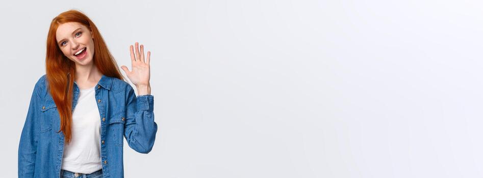 amigable, alegre y saliente bonito pelirrojo niña ondulación palmera, diciendo Hola, saludo equipo miembro, inclinación cabeza y sonriente alegremente, bonito reunirse tú, decir Hola y en pie blanco antecedentes foto