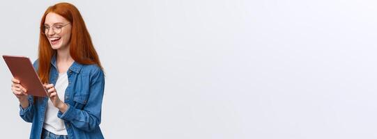 Waist-up porrtrait happy cheerful redhead girlfriend talking to partner using internet video-call service, laughing happily, having fun, smiling at gadget camera, standing white background photo