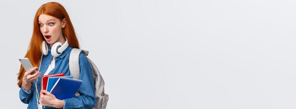conmocionado y asombrado, jadeando Sin palabras pelirrojo hembra estudiante con mochila y cuadernos, curioso a teléfono inteligente pantalla tembló abierto boca y popular ojos móvil monitor foto