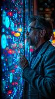 A man with a beard and glasses looks out of a window at a computer screen photo
