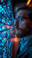 A man with a beard and glasses is looking at a blue and purple computer screen photo