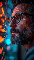 A man wearing eyewear and a beard is attentively gazing at a computer screen photo