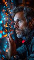 A man looking out a window has a beard and is focused on a computer screen photo