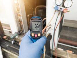 Professional engineer wearing blue gloves using thermo gun for temperature check on the hvac air cinditioning syatem. Temperature check concept on the compressor, condensor , refrigerant system hvac. photo