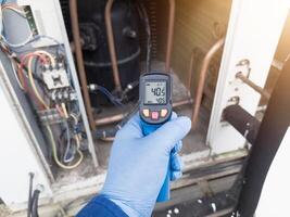Professional engineer wearing blue gloves using thermo gun for temperature check on the hvac air cinditioning syatem. Temperature check concept on the compressor, condensor , refrigerant system hvac. photo
