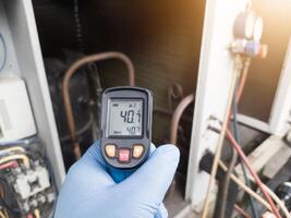 Professional engineer wearing blue gloves using thermo gun for temperature check on the hvac air cinditioning syatem. Temperature check concept on the compressor, condensor , refrigerant system hvac. photo