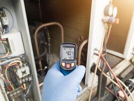 Professional engineer wearing blue gloves using thermo gun for temperature check on the hvac air cinditioning syatem. Temperature check concept on the compressor, condensor , refrigerant system hvac. photo