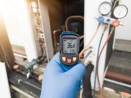 Professional engineer wearing blue gloves using thermo gun for temperature check on the hvac air cinditioning syatem. Temperature check concept on the compressor, condensor , refrigerant system hvac. photo