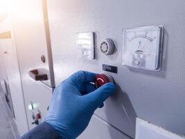 A hand engineer with blue gloves reset the Emergency Push Botton on panel control after used when emergency condition.How to use emergency switch on panel control power plant. photo