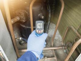 Professional engineer wearing blue gloves using thermo gun for temperature check on the hvac air cinditioning syatem. Temperature check concept on the compressor, condensor , refrigerant system hvac. photo