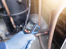 Professional engineer wearing blue gloves using thermo gun for temperature check on the hvac air cinditioning syatem. Temperature check concept on the compressor, condensor , refrigerant system hvac. photo