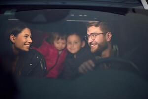 In the nighttime hours, a happy family enjoys playful moments together inside a car as they journey on a nocturnal road trip, illuminated by the glow of headlights and filled with laughter and joy photo