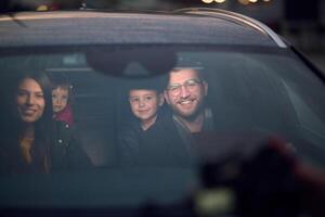 In the nighttime hours, a happy family enjoys playful moments together inside a car as they journey on a nocturnal road trip, illuminated by the glow of headlights and filled with laughter and joy photo
