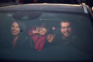 In the nighttime hours, a happy family enjoys playful moments together inside a car as they journey on a nocturnal road trip, illuminated by the glow of headlights and filled with laughter and joy photo