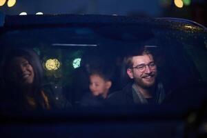In the nighttime hours, a happy family enjoys playful moments together inside a car as they journey on a nocturnal road trip, illuminated by the glow of headlights and filled with laughter and joy photo