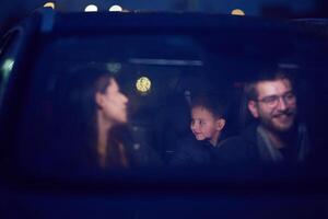 In the nighttime hours, a happy family enjoys playful moments together inside a car as they journey on a nocturnal road trip, illuminated by the glow of headlights and filled with laughter and joy photo