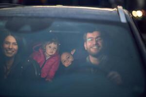 In the nighttime hours, a happy family enjoys playful moments together inside a car as they journey on a nocturnal road trip, illuminated by the glow of headlights and filled with laughter and joy photo