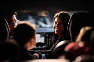 In the nighttime hours, a happy family enjoys playful moments together inside a car as they journey on a nocturnal road trip, illuminated by the glow of headlights and filled with laughter and joy photo
