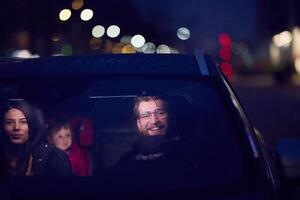 In the nighttime hours, a happy family enjoys playful moments together inside a car as they journey on a nocturnal road trip, illuminated by the glow of headlights and filled with laughter and joy photo
