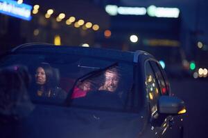 In the nighttime hours, a happy family enjoys playful moments together inside a car as they journey on a nocturnal road trip, illuminated by the glow of headlights and filled with laughter and joy photo