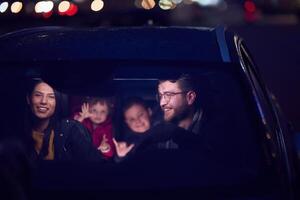 In the nighttime hours, a happy family enjoys playful moments together inside a car as they journey on a nocturnal road trip, illuminated by the glow of headlights and filled with laughter and joy photo