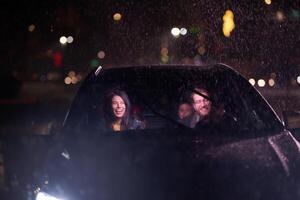 In the midst of a nighttime journey, a happy family enjoys playful moments inside a car as they travel through rainy weather, illuminated by the glow of headlights, laughter, and bonding photo