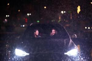 In the midst of a nighttime journey, a happy family enjoys playful moments inside a car as they travel through rainy weather, illuminated by the glow of headlights, laughter, and bonding photo