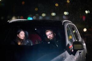 In the midst of a nighttime journey, a happy family enjoys playful moments inside a car as they travel through rainy weather, illuminated by the glow of headlights, laughter, and bonding photo