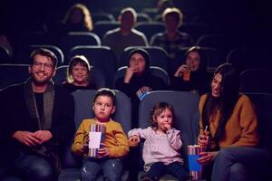 A modern family enjoys quality time together at the cinema, indulging in popcorn while watching a movie with their children photo