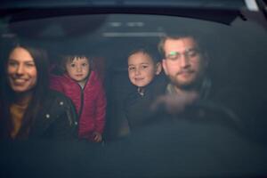 In the nighttime hours, a happy family enjoys playful moments together inside a car as they journey on a nocturnal road trip, illuminated by the glow of headlights and filled with laughter and joy photo