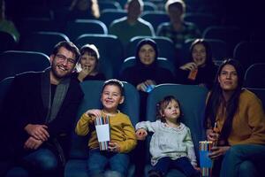 A modern family enjoys quality time together at the cinema, indulging in popcorn while watching a movie with their children photo