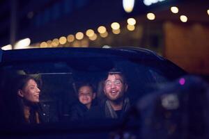 In the nighttime hours, a happy family enjoys playful moments together inside a car as they journey on a nocturnal road trip, illuminated by the glow of headlights and filled with laughter and joy photo