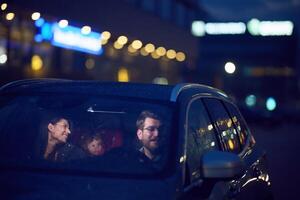 In the nighttime hours, a happy family enjoys playful moments together inside a car as they journey on a nocturnal road trip, illuminated by the glow of headlights and filled with laughter and joy photo
