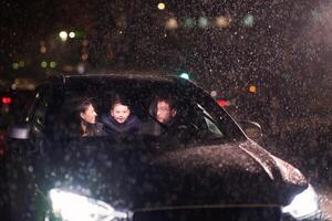 In the midst of a nighttime journey, a happy family enjoys playful moments inside a car as they travel through rainy weather, illuminated by the glow of headlights, laughter, and bonding photo