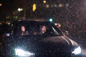 In the midst of a nighttime journey, a happy family enjoys playful moments inside a car as they travel through rainy weather, illuminated by the glow of headlights, laughter, and bonding photo