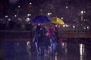 In the midst of a rainy urban night, a happy couple takes their children on a stroll through the city streets, heading towards the cinema for a delightful family movie outing photo