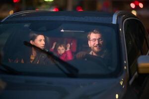 In the nighttime hours, a happy family enjoys playful moments together inside a car as they journey on a nocturnal road trip, illuminated by the glow of headlights and filled with laughter and joy photo