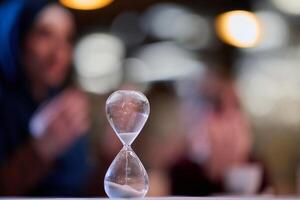 A symbolic hourglass counts down the time to iftar meal, while in the background, an Islamic family devoutly prays, capturing a poignant moment of spiritual connection and anticipation during Ramadan photo