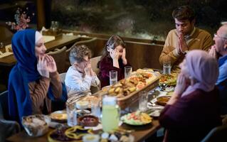 In a modern restaurant setting, a European Islamic family comes together for iftar during Ramadan, engaging in prayer before the meal, uniting tradition and contemporary practices in a celebration of photo